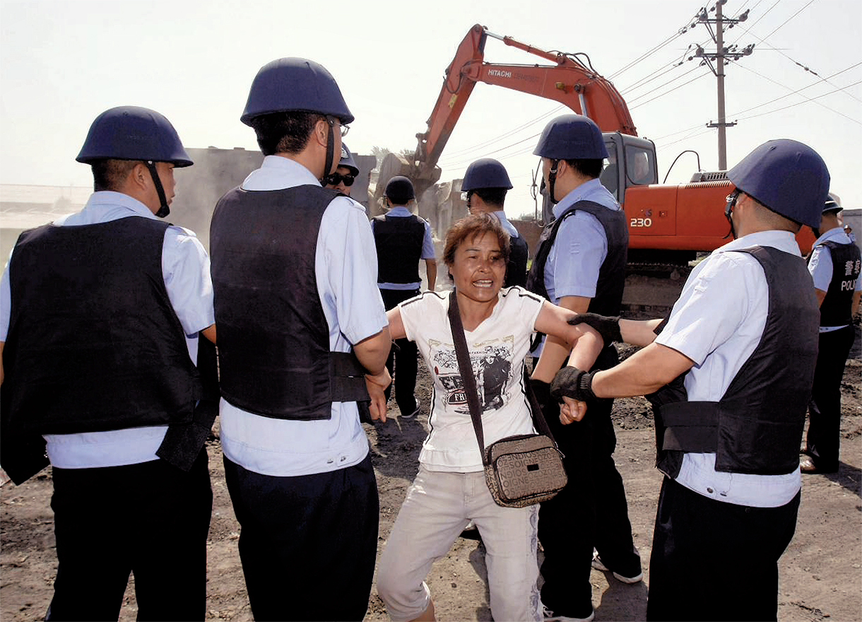 Une femme, maintenue par les forces de l’ordre, proteste lors de la démolition de bâtiments à Changchun en juin 2010